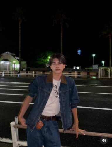 夜、ヤシの木と駐車場を背景にしたYUKI、奥に青くライトアップされたタワーが見える